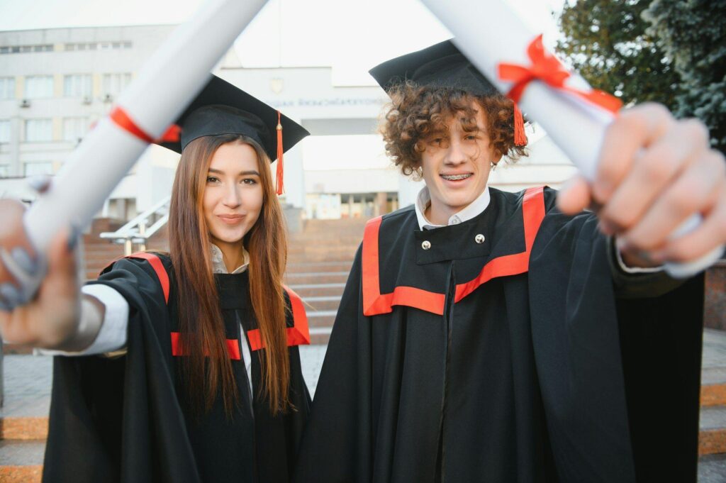 Portrait of happy graduates. Two friends in graduation caps and gowns standing outside university