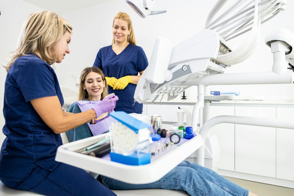 Female dentist with assistant working in dental clinic examining patient teeth.