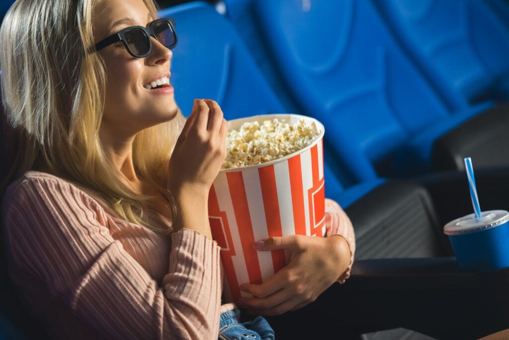 side view of smiling woman in 3d glasses with popcorn watching film alone in cinema