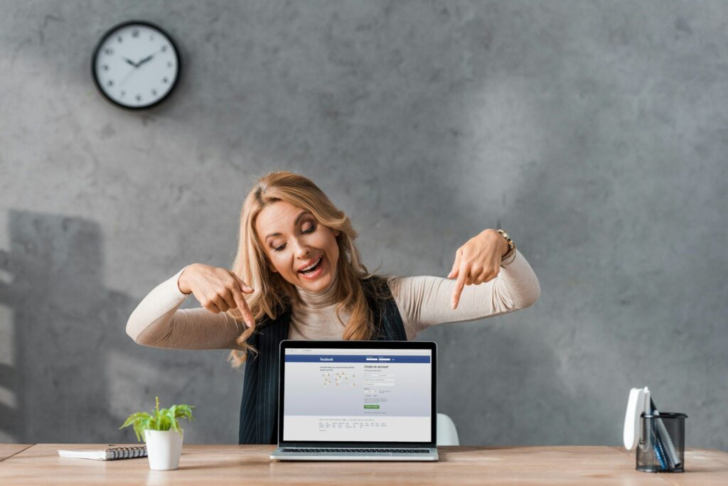 KYIV, UKRAINE - AUGUST 16, 2019: smiling businesswoman pointing with fingers at laptop facebook