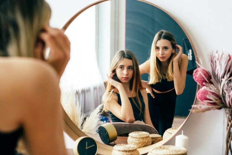 Two beautiful teenage girls look at their reflection in the mirror. Young narcissistic women.