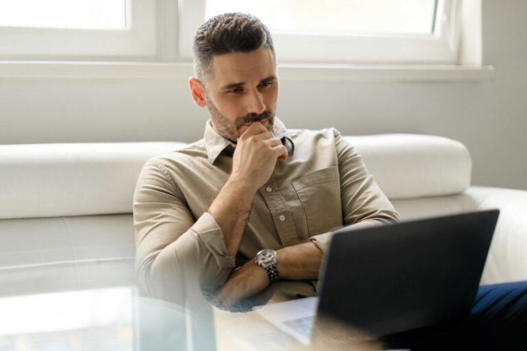 Focused thoughtful businessman using laptop and thinking of project, making decision, looking at