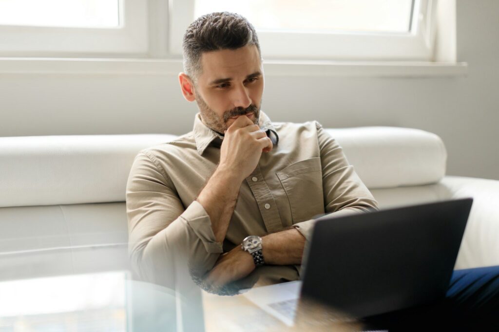 Focused thoughtful businessman using laptop and thinking of project, making decision, looking at