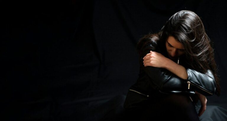 Young woman in a black leather jacket, sad and lonely in a dark room. Depression and grief