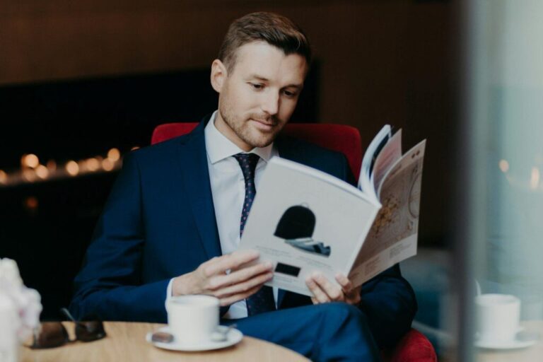 Concentrated businessman looks attentively in menu while sits in cozy restaurant, drinks coffee