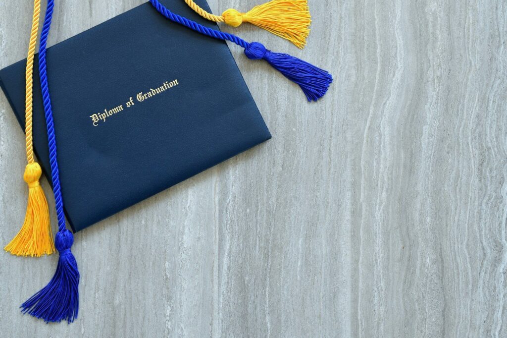 Flat lay of a Diploma of Graduation with honor cords on a simple wooden background.