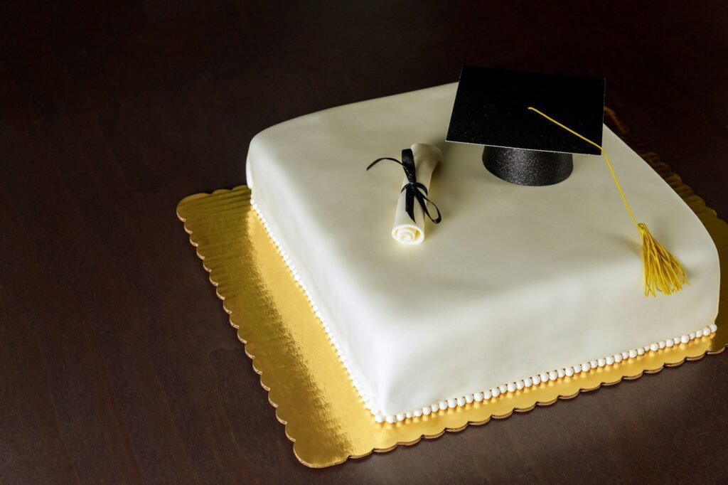 Graduation white cake with cap on the top and diploma decor.