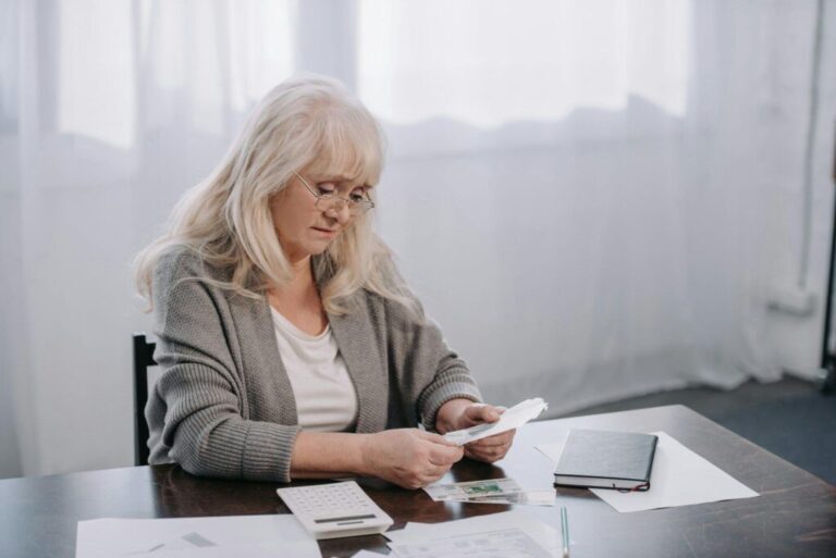 senior woman sitting at table with paperwork and counting money