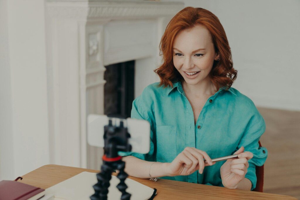 Social media influencer blogger keeps mobile phone on tripod, looks gladfully at camera