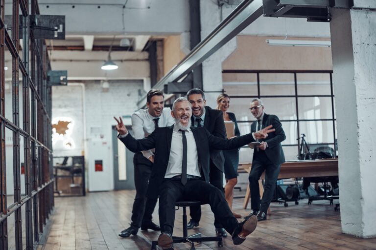 Playful businessmen pushing their boss on the office chair while running in the hallway