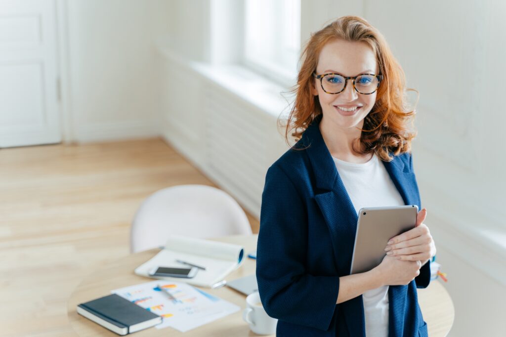 Prosperous female leader of working team holds digital tablet device, develops business ideas