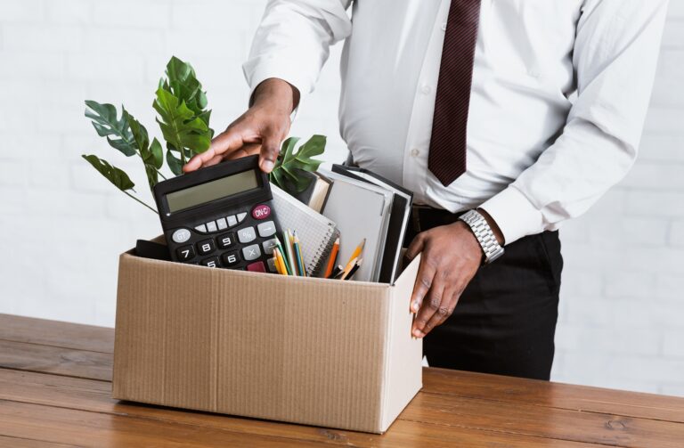 Unrecognizable black guy collecting his office stuff into carton box. Economic crisis and